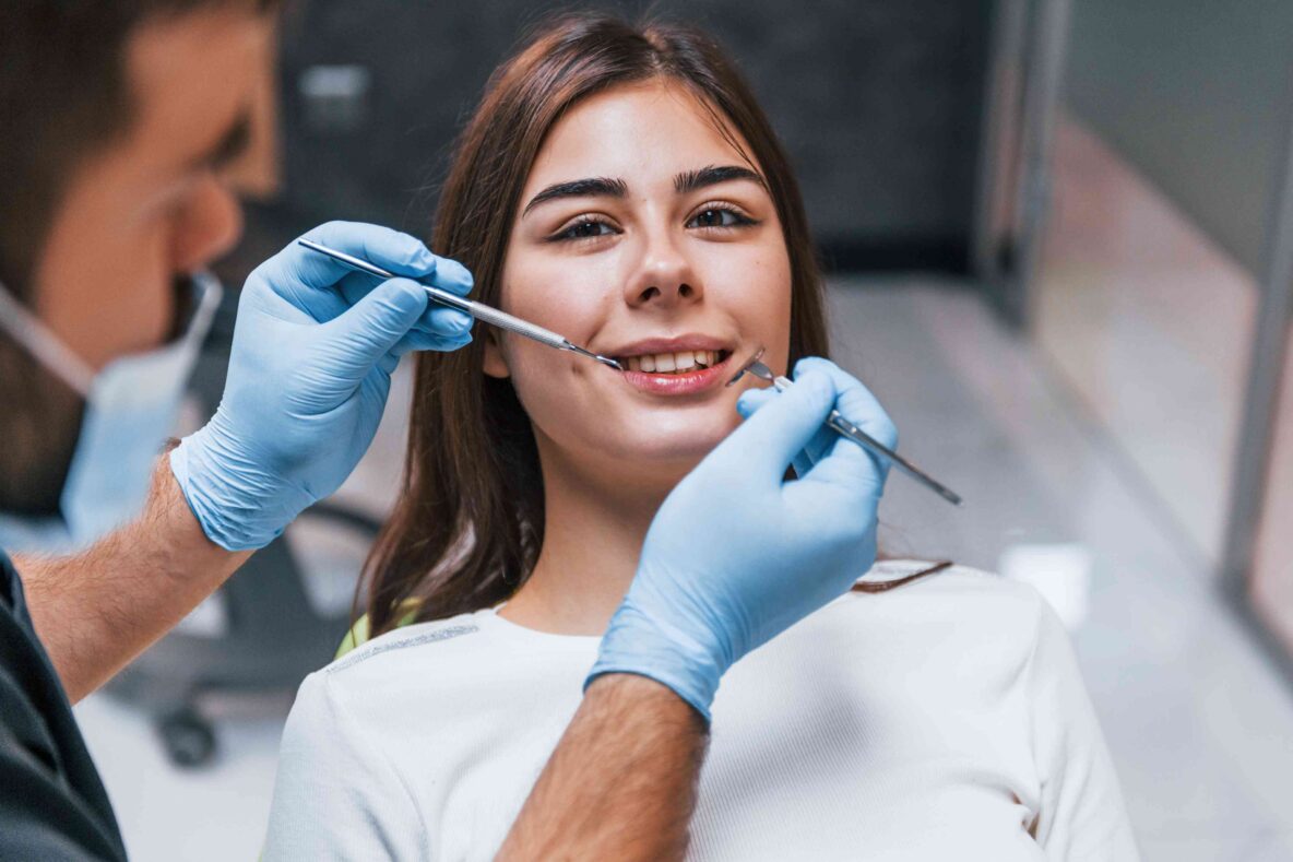 Dentist examining patient’s teeth with dental tools.